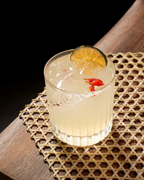 Pale margarita on ice in a ribbed glass with a chili-salt rim, a dried lime wheel and red chili