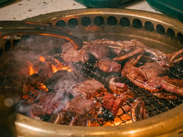 Short ribs and beef cubes searing over open flames and smoke on a brass tabletop grill