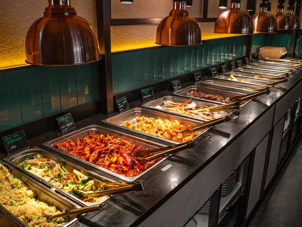 Hot buffet line under copper heat lamps: fried rice, stir-fried vegetables, crawfish and a long row of steel pans